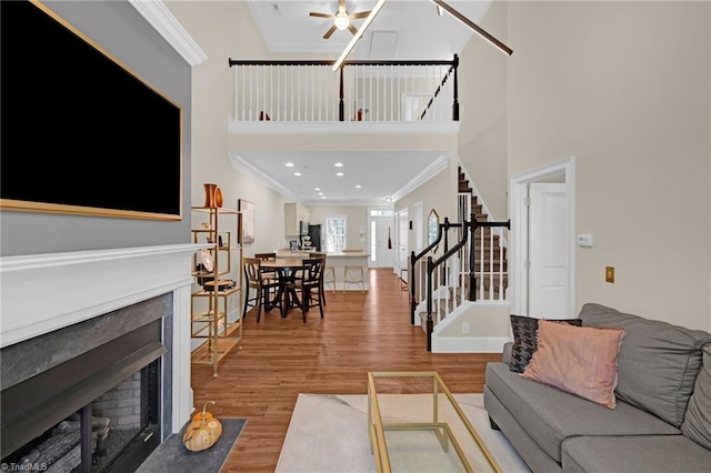 living room featuring hardwood / wood-style floors, ceiling fan, ornamental molding, and a towering ceiling