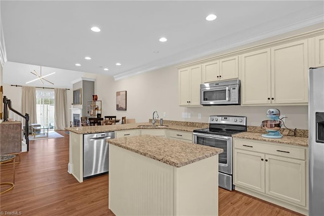 kitchen with a center island, crown molding, cream cabinetry, kitchen peninsula, and stainless steel appliances