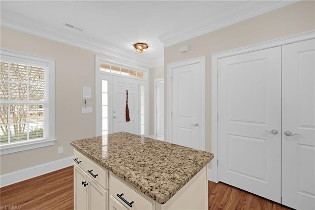 kitchen with a center island, crown molding, dark hardwood / wood-style floors, light stone counters, and white cabinetry