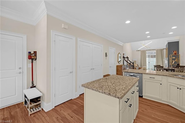 kitchen with light stone countertops, light hardwood / wood-style flooring, stainless steel dishwasher, and a kitchen island