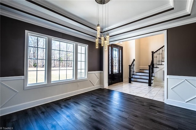 unfurnished room featuring a wainscoted wall, stairway, ornamental molding, wood finished floors, and a tray ceiling