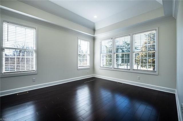 unfurnished room with a tray ceiling, dark wood-style flooring, visible vents, and baseboards