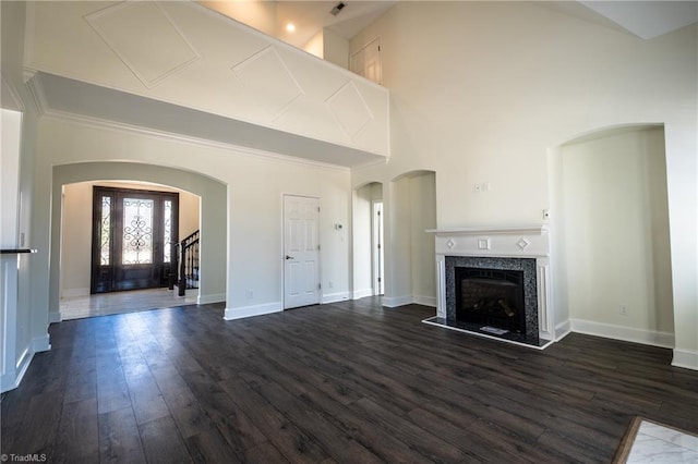 unfurnished living room with dark wood-style floors, arched walkways, a fireplace with raised hearth, a towering ceiling, and baseboards