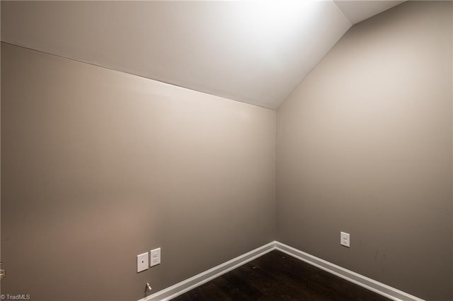 unfurnished room featuring dark wood-style flooring, vaulted ceiling, and baseboards