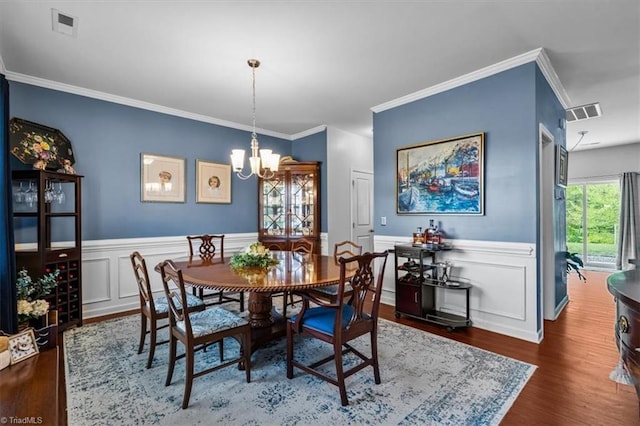dining space with an inviting chandelier, ornamental molding, wood finished floors, and visible vents