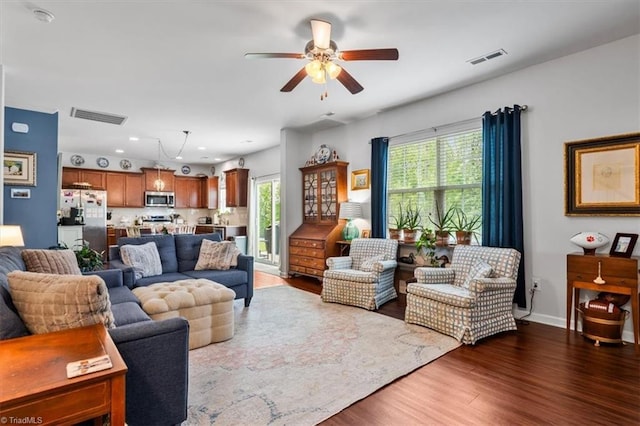 living room with a healthy amount of sunlight, visible vents, a ceiling fan, and dark wood finished floors