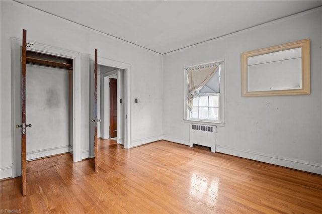 unfurnished bedroom with radiator heating unit, baseboards, and light wood-type flooring