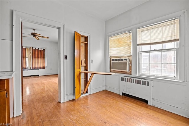 unfurnished room featuring cooling unit, light wood-style flooring, radiator, and ceiling fan