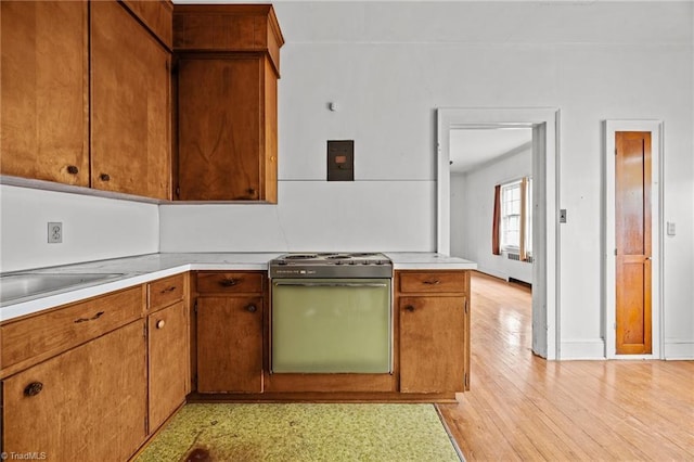 kitchen featuring light countertops, electric range, brown cabinetry, and light wood-style flooring