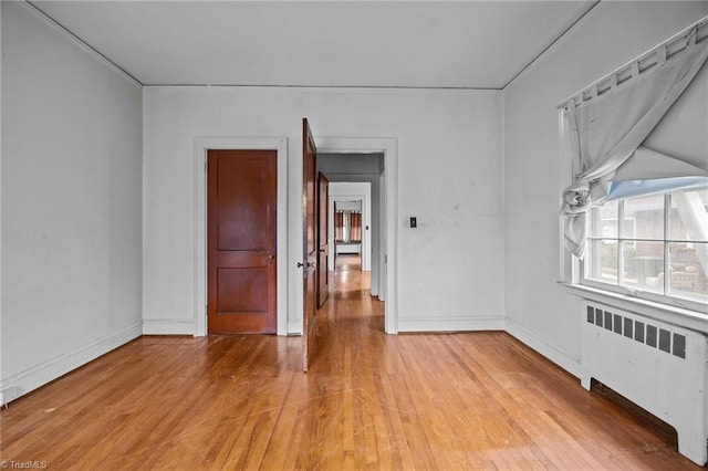 spare room with baseboards, radiator, and light wood-style flooring