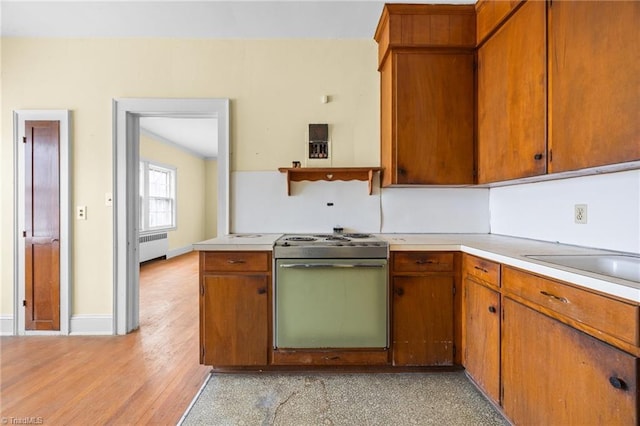 kitchen featuring radiator, baseboards, light countertops, electric stove, and brown cabinets