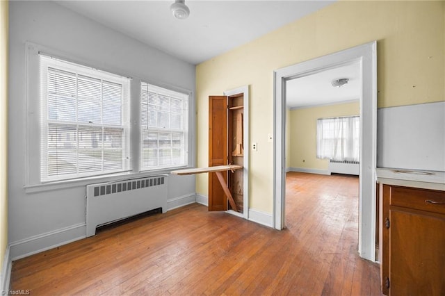 unfurnished bedroom with hardwood / wood-style flooring, radiator, and baseboards