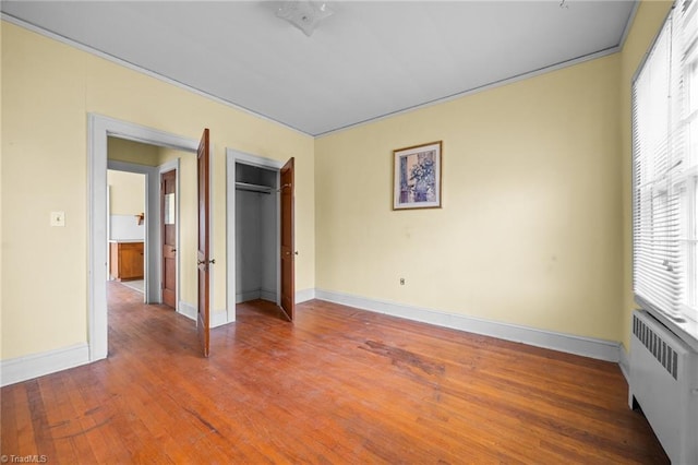 unfurnished bedroom with a closet, baseboards, radiator, and hardwood / wood-style floors