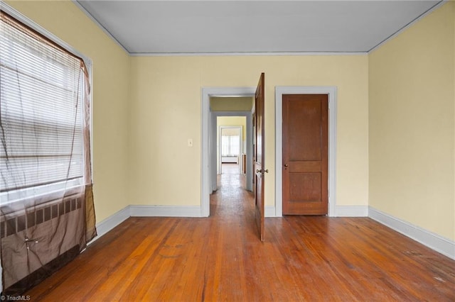 spare room featuring radiator, wood finished floors, baseboards, and ornamental molding