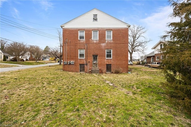 back of house featuring brick siding, a lawn, and entry steps