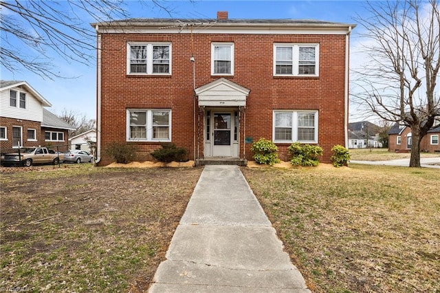 view of front facade with brick siding, a chimney, and a front yard