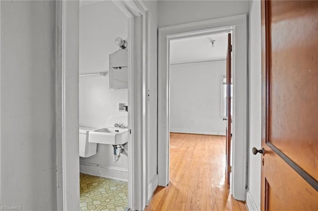 hall featuring light wood-style flooring, baseboards, and a sink