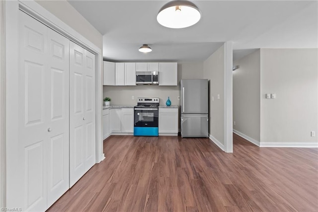 kitchen with appliances with stainless steel finishes, white cabinets, wood finished floors, baseboards, and light stone counters