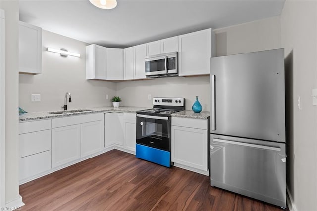 kitchen with appliances with stainless steel finishes, a sink, dark wood-style flooring, white cabinets, and light stone countertops