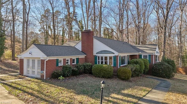 view of front facade featuring roof with shingles, brick siding, a chimney, and a front lawn