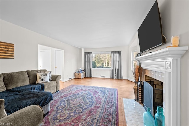 living area with light wood-type flooring, baseboards, visible vents, and a tiled fireplace