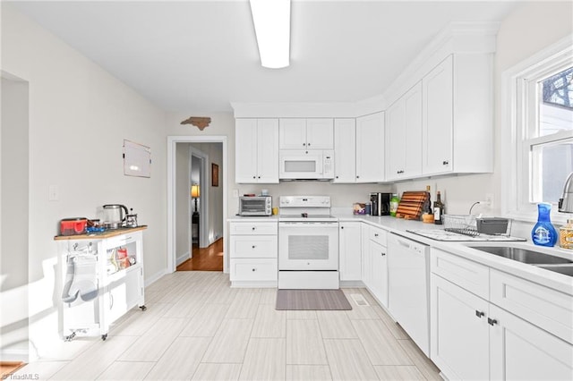 kitchen featuring white appliances, a toaster, white cabinets, light countertops, and a sink