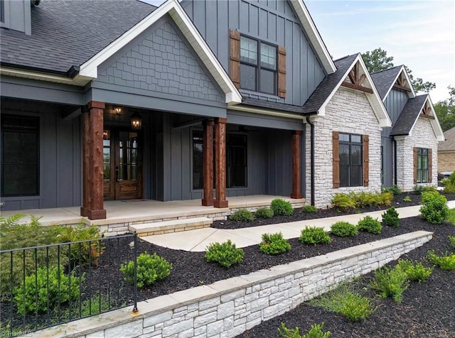 entrance to property with stone siding, roof with shingles, french doors, a porch, and board and batten siding