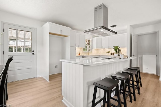 317 Benbow Dr, East Bend, NC 27018 - kitchen featuring island exhaust hood, backsplash, white cabinets, light countertops, and healthy amount of natural light