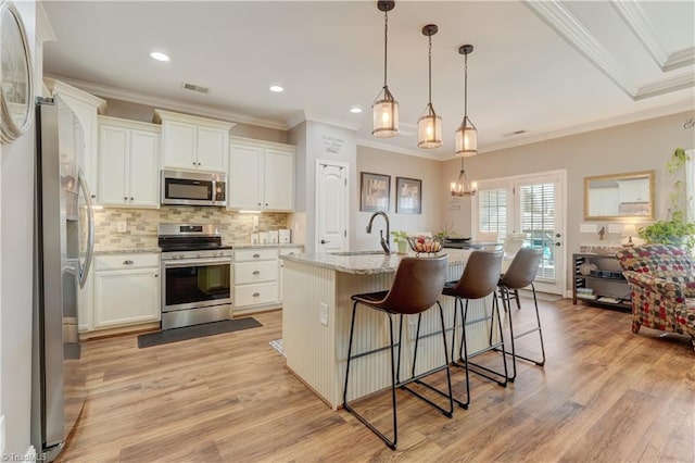 kitchen with light stone countertops, appliances with stainless steel finishes, a kitchen island with sink, white cabinets, and light hardwood / wood-style floors