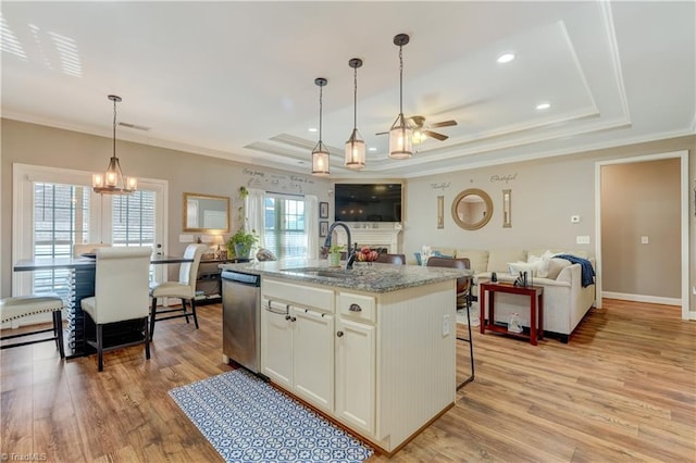 kitchen featuring sink, a raised ceiling, stainless steel dishwasher, light hardwood / wood-style floors, and a kitchen island with sink