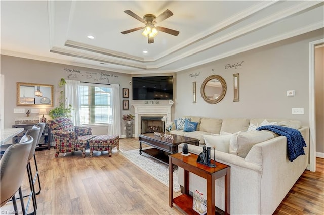 living room with a raised ceiling, ceiling fan, ornamental molding, and hardwood / wood-style flooring