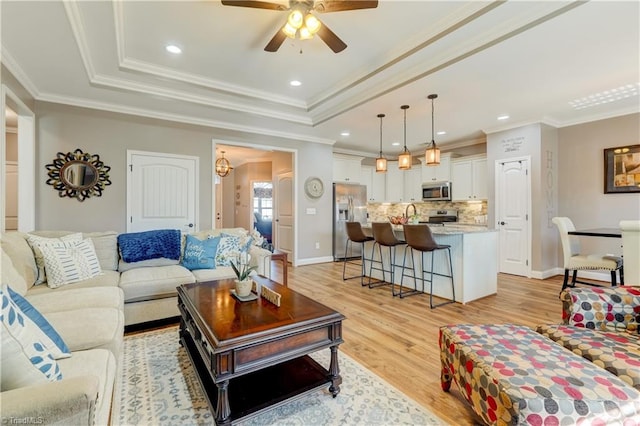 living room with a raised ceiling, crown molding, light hardwood / wood-style flooring, and ceiling fan with notable chandelier