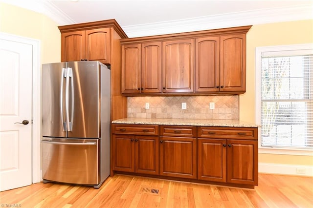 kitchen with light hardwood / wood-style flooring, stainless steel fridge, tasteful backsplash, light stone countertops, and ornamental molding