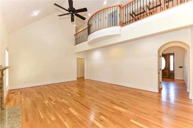 unfurnished living room with ceiling fan, high vaulted ceiling, light hardwood / wood-style floors, and a stone fireplace