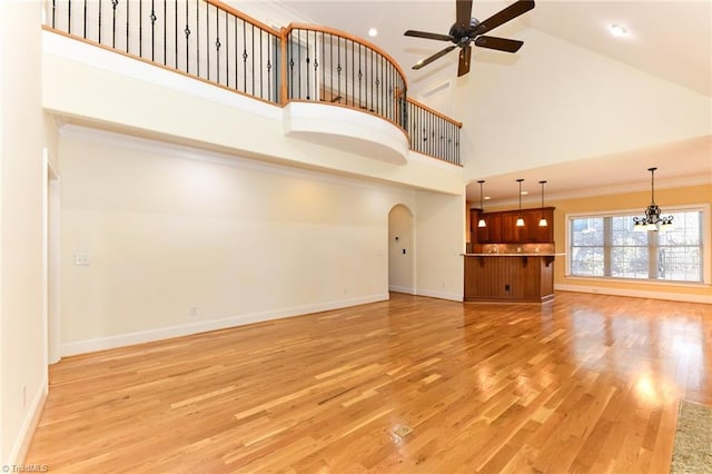 unfurnished living room with crown molding, ceiling fan with notable chandelier, light hardwood / wood-style flooring, and high vaulted ceiling