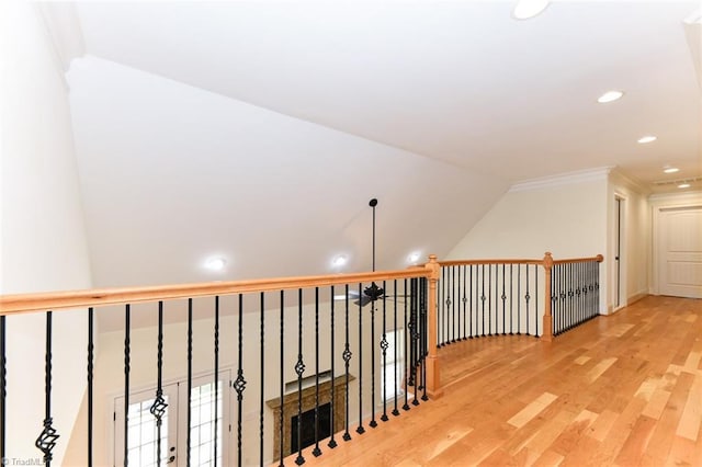 corridor featuring wood-type flooring, ornamental molding, and vaulted ceiling