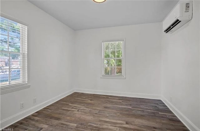 empty room featuring an AC wall unit, baseboards, and dark wood finished floors