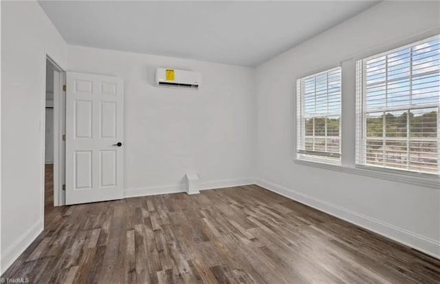 empty room with baseboards, wood finished floors, and a wall unit AC