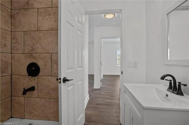 full bathroom with a tile shower, wood finished floors, vanity, and baseboards