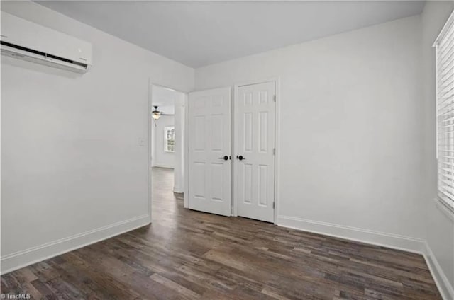 unfurnished bedroom featuring dark wood-type flooring, baseboards, and a wall mounted air conditioner
