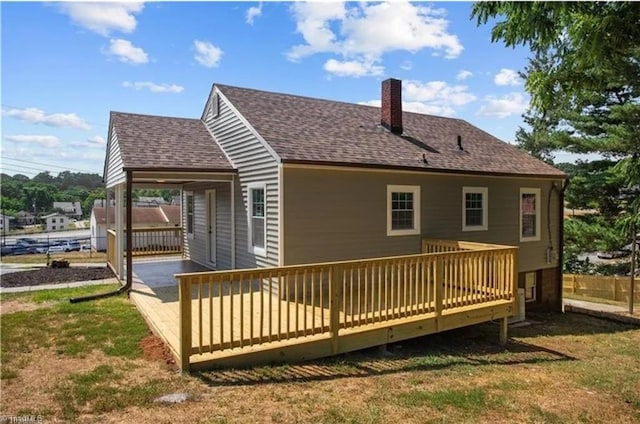 back of property featuring a shingled roof, a deck, a lawn, a chimney, and fence
