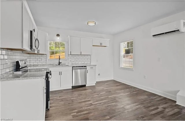 kitchen featuring tasteful backsplash, dark wood-style floors, a wall unit AC, appliances with stainless steel finishes, and a sink