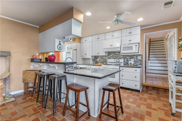 kitchen featuring kitchen peninsula, a kitchen bar, white appliances, and white cabinetry