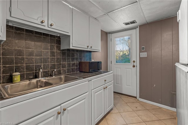 kitchen with a paneled ceiling, tasteful backsplash, sink, light tile patterned floors, and white cabinetry