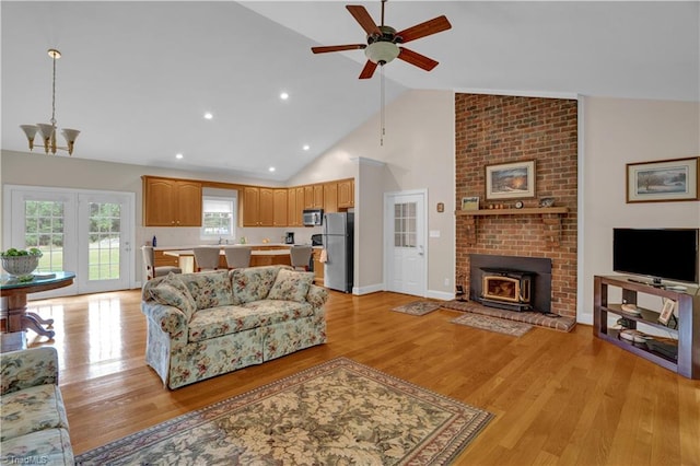 living room featuring light hardwood / wood-style flooring, brick wall, high vaulted ceiling, ceiling fan, and a brick fireplace