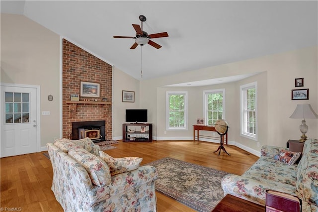 living room with ceiling fan, light hardwood / wood-style flooring, brick wall, a brick fireplace, and vaulted ceiling