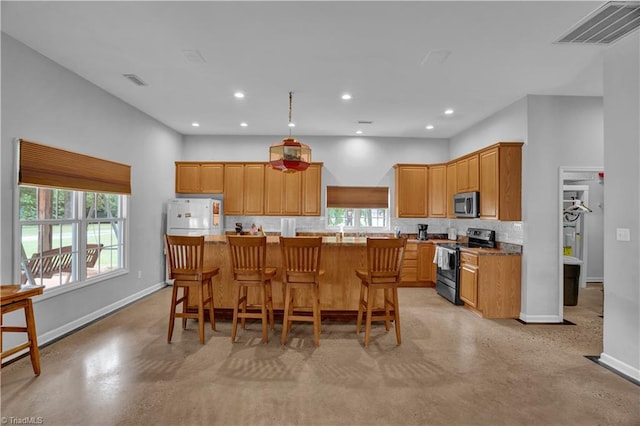 kitchen with appliances with stainless steel finishes, backsplash, light stone counters, a breakfast bar area, and a center island