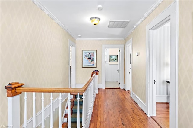 hallway featuring wood finished floors, baseboards, visible vents, ornamental molding, and an upstairs landing