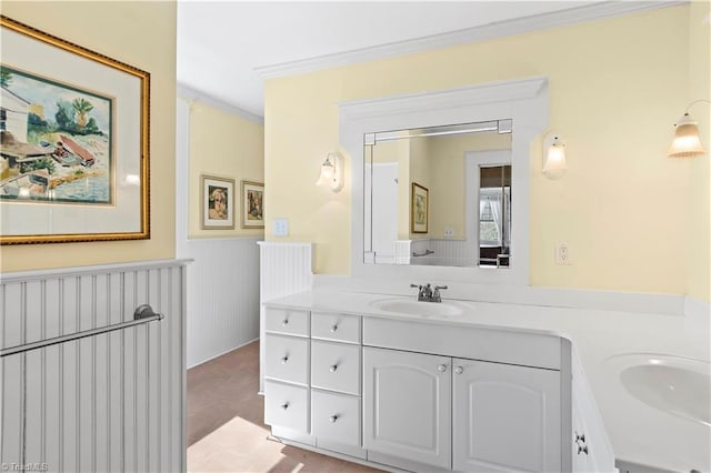 bathroom with a sink, a wainscoted wall, double vanity, and crown molding