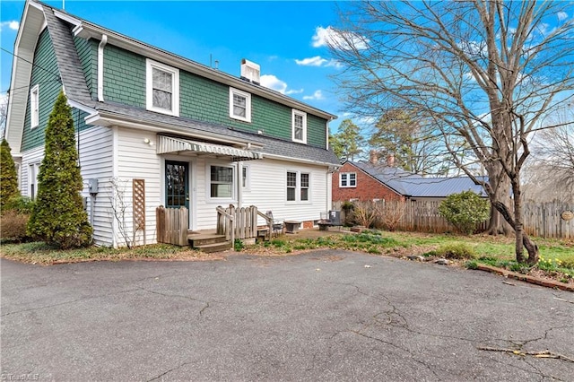 view of front of house with a shingled roof, a gambrel roof, a chimney, and fence